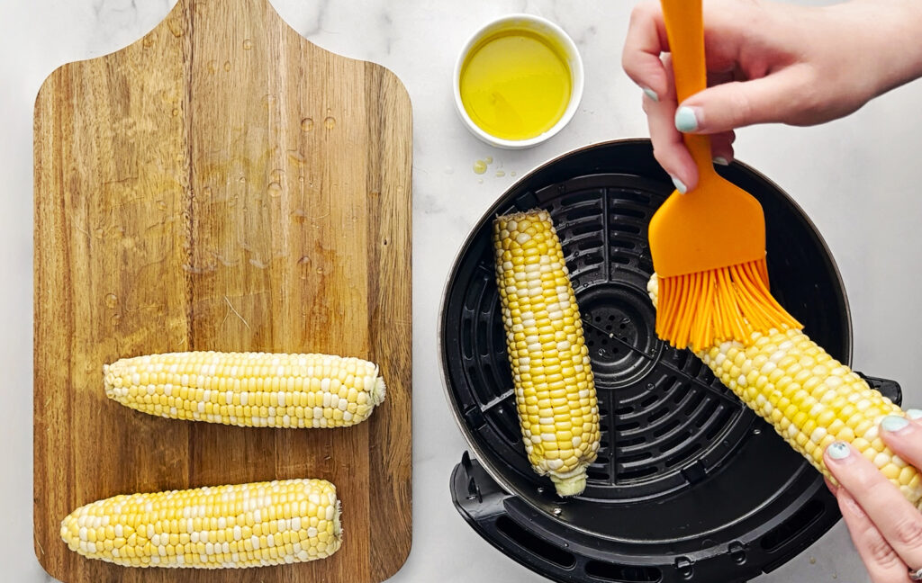 Spreading Olive Oil on Ears of Corn to Prepare for Air Fryer