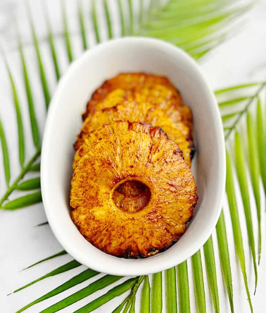 Air Fried Pineapple Rings in White Serving Dish with Tropical Green Leaves in the Background