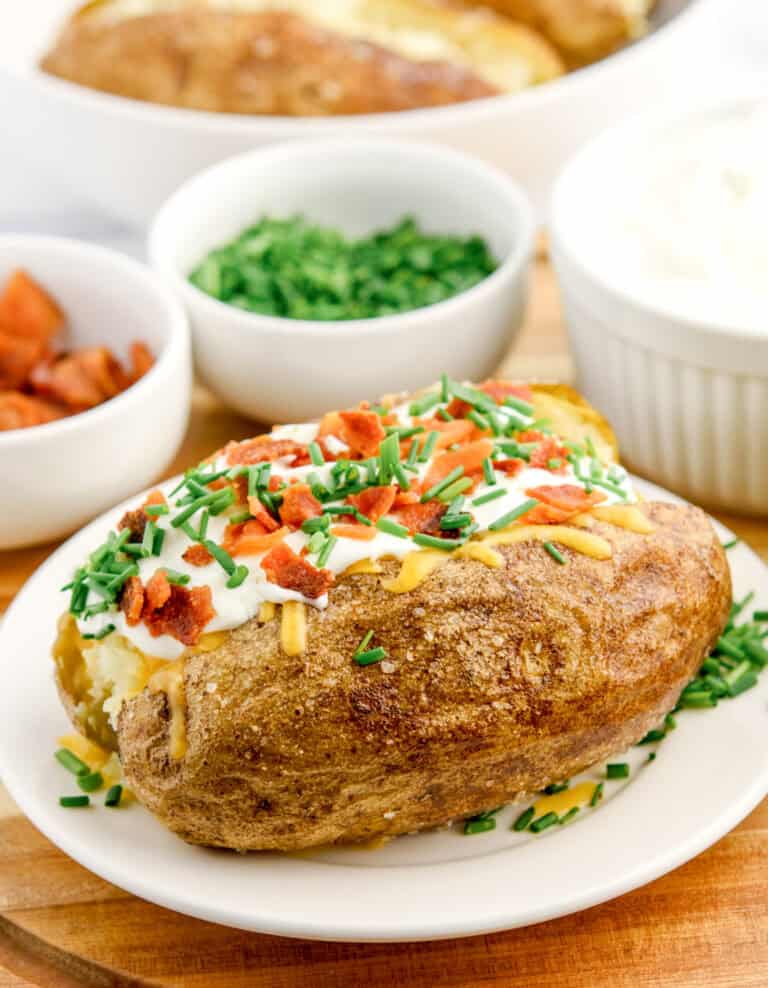 Baked Potato with Sour Cream, Cheese, Green Onions, and Bacon with Bowls of Toppings in the Back