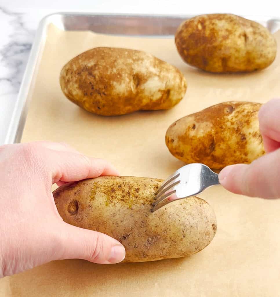 Poking Fork into Raw Potatoes on Baking Sheet with Parchment Paper