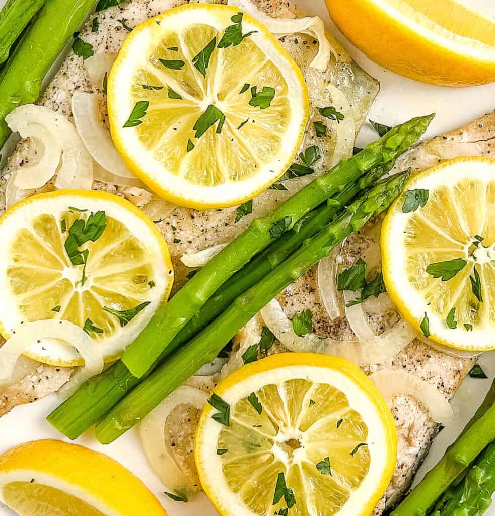 Plated Trout with Asparagus, Garnished with Lemon, Herbs, and Onions