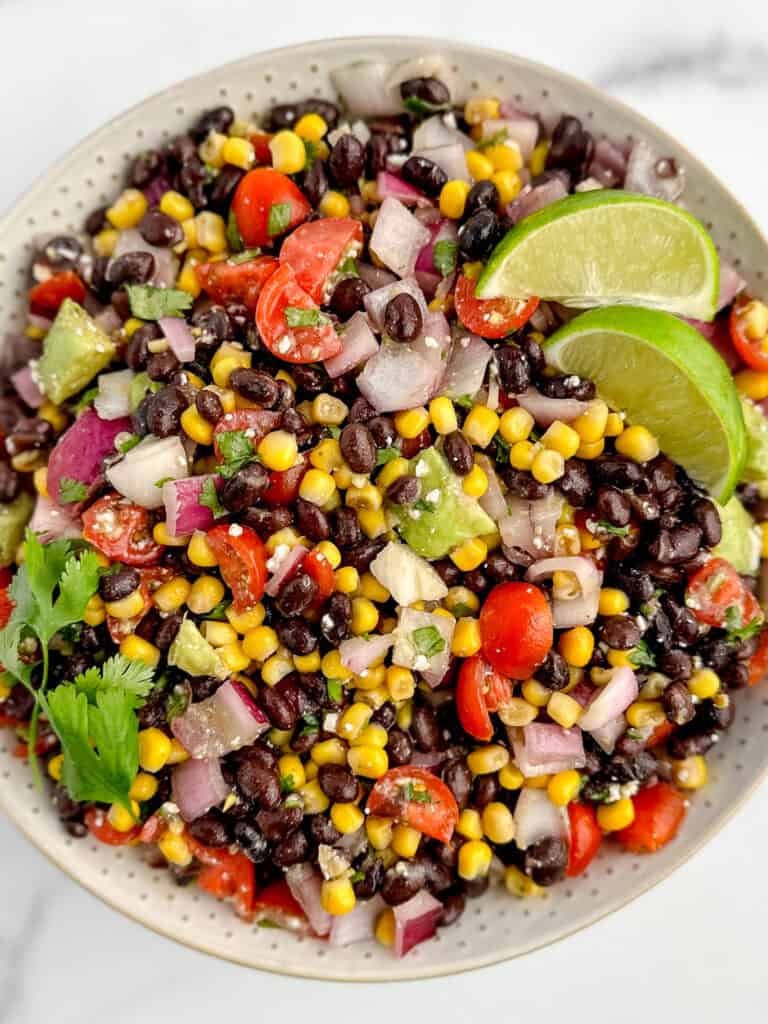 Finished Black Bean Salad in Serving Bowl with Garnishes of Lime and Cilantro Leaves