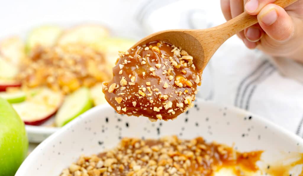 Wooden Spoon Serving Scoop of Caramel Apple Dip in Speckled White Bowl