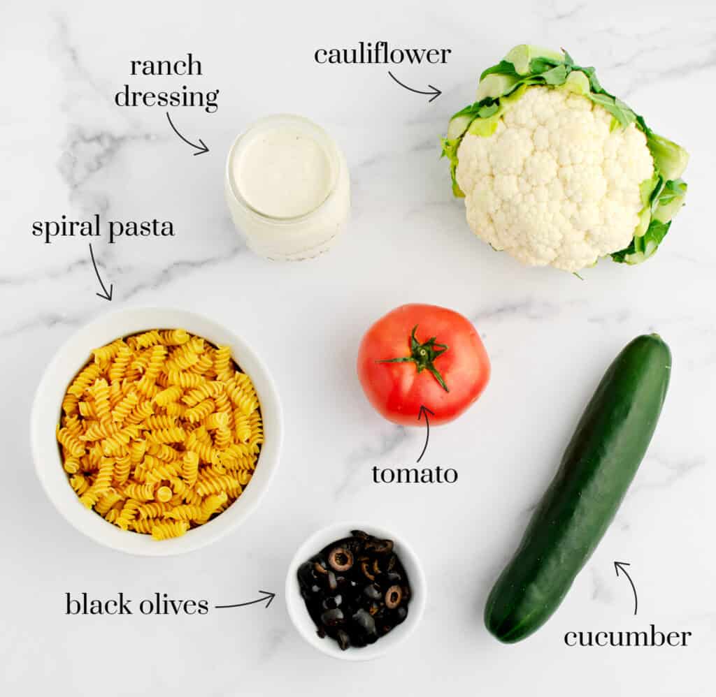 Spiral Pasta, Tomato, Cucumber, Head of Cauliflower, Olives, and Ranch on White Marble Counter