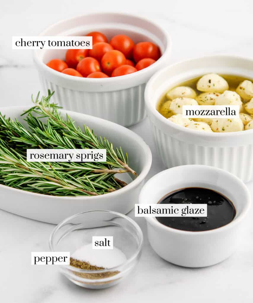 Rosemary, Cherry Tomatoes, Mozarella Balls, Balsamic Glaze, and Salt and Pepper in Bowls on White Marble Surface