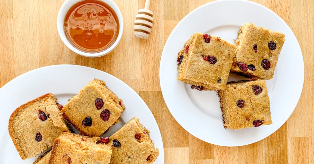 Slices of Cranberry Cinnamon Cornbread on Plates with Bowl of Honey