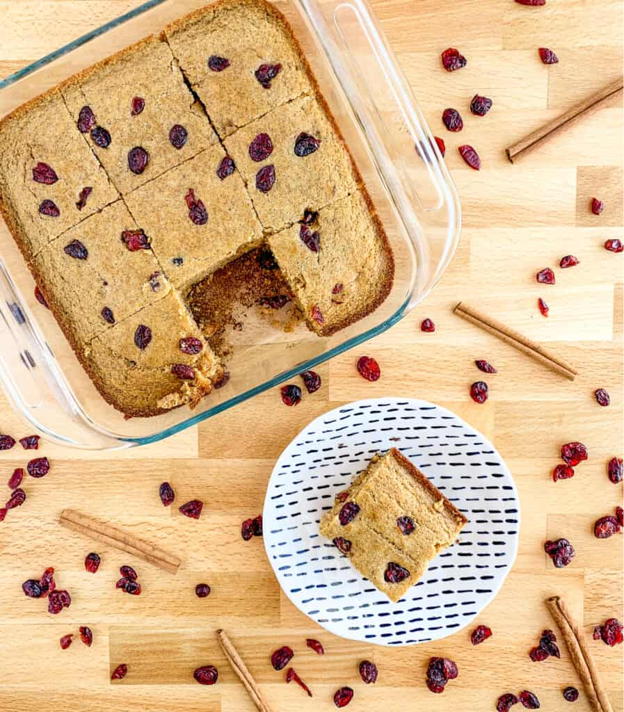 Slice of Cornbread Cut Out of Pan on Plate with Dried Cranberries and CInnamon Surrounding