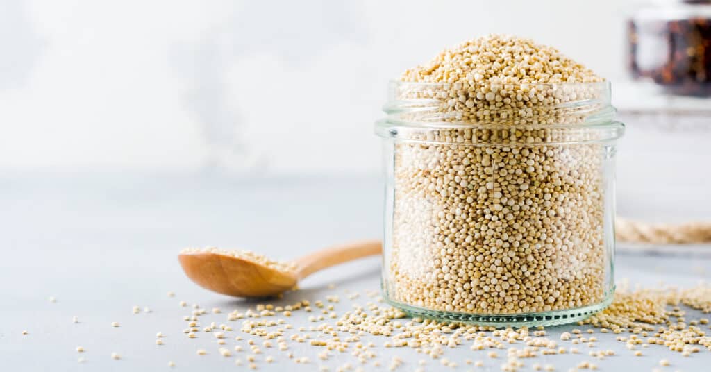 Raw Quinoa in a Glass Jar with Quinoa and a Spoon Beside in on the Countertop