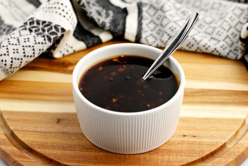 Homemade Teriyaki Sauce in Bowl on Wooden Surface with Kitchen Towel in Background