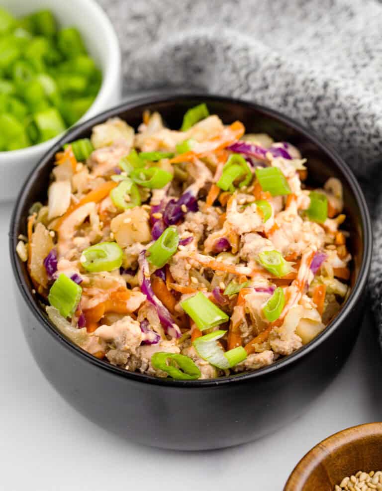 Egg Roll in a Bowl in a Black Bowl with Chopped Green Onions in a White Bowl in the Background with a Kitchen Towel