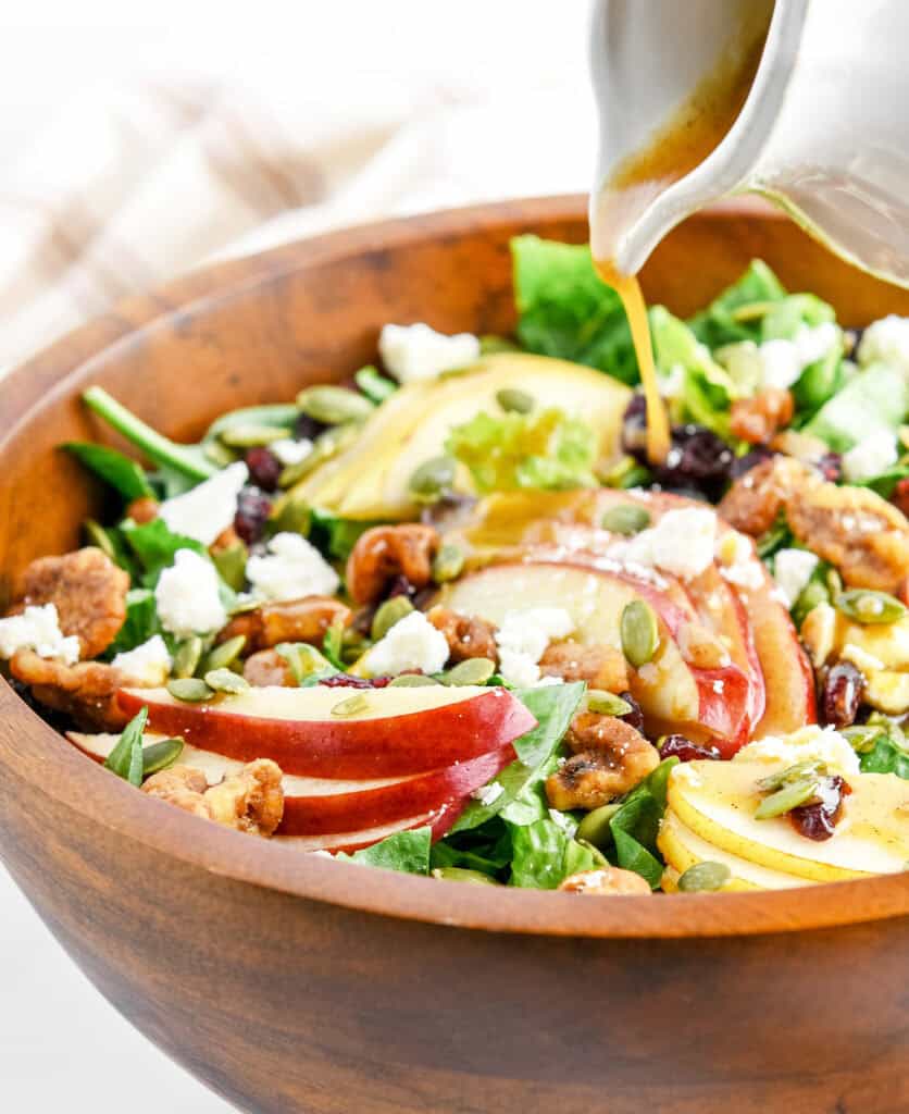 Pouring Dressing onto Fall Salad in Wooden Bowl
