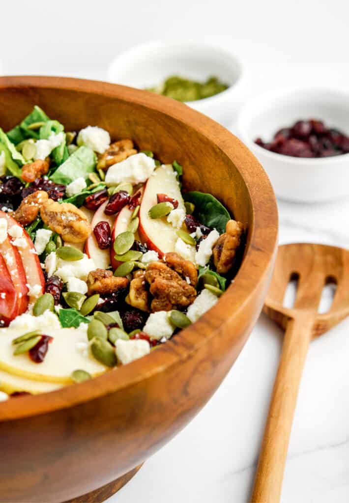 Fall Salad in Wooden Bowl with Wooden Spoon on Counter Beside It