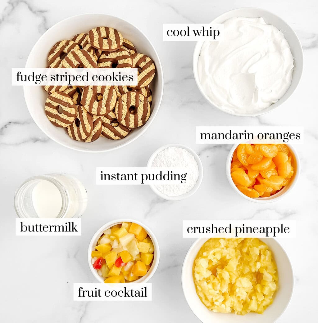 Striped Cookies, Cool Whip, Oranges, Pineapple, Fruit Cocktail, Pudding Mix, and Buttermilk in Bowls on Marble Surface