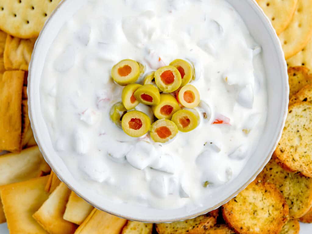 Top Down Green Olive Dip in Bowl with Crackers, Pita Chips, and Bagel Chips