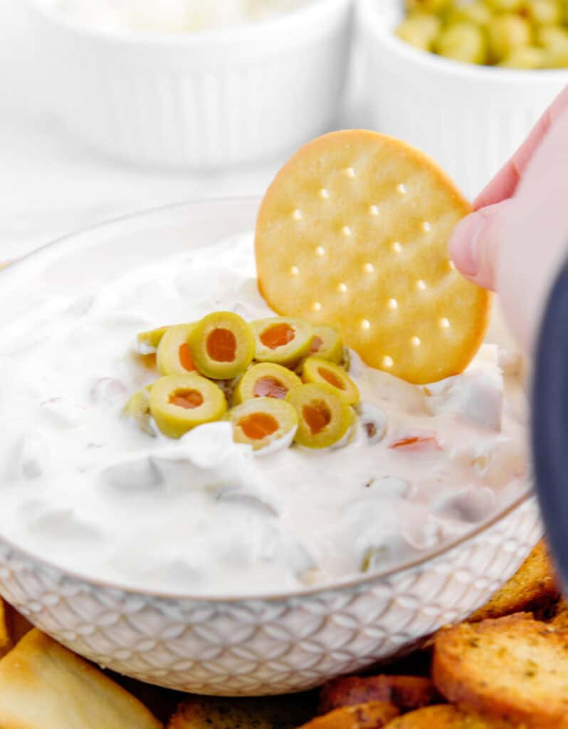Hand Dipping Cracker Into Olive Dip