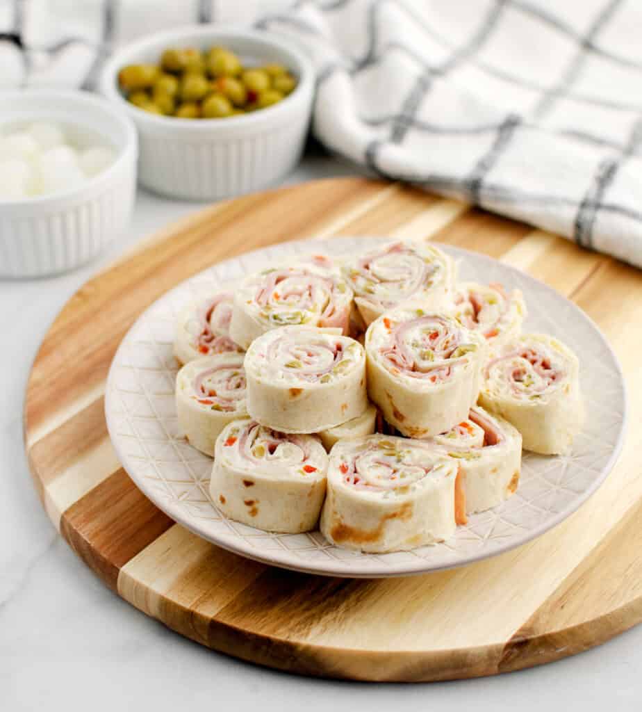 Green Olive Rollups on Serving Plate on Wooden Surface with Bowl of Olives and Cocktail Onions in the Background