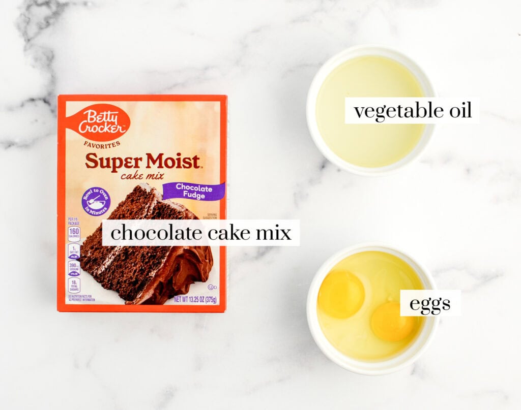 Box of Chocolate Cake, Bowl of Eggs, Bowl of Oil on White Marble Surface