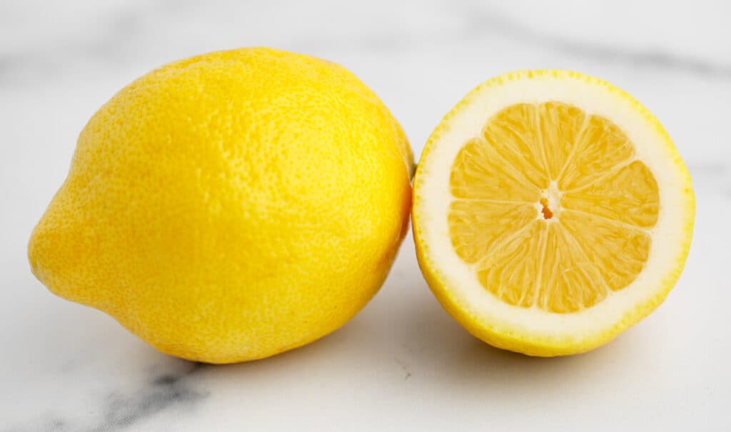 Whole Lemon and Half Lemon on White Marble Surface