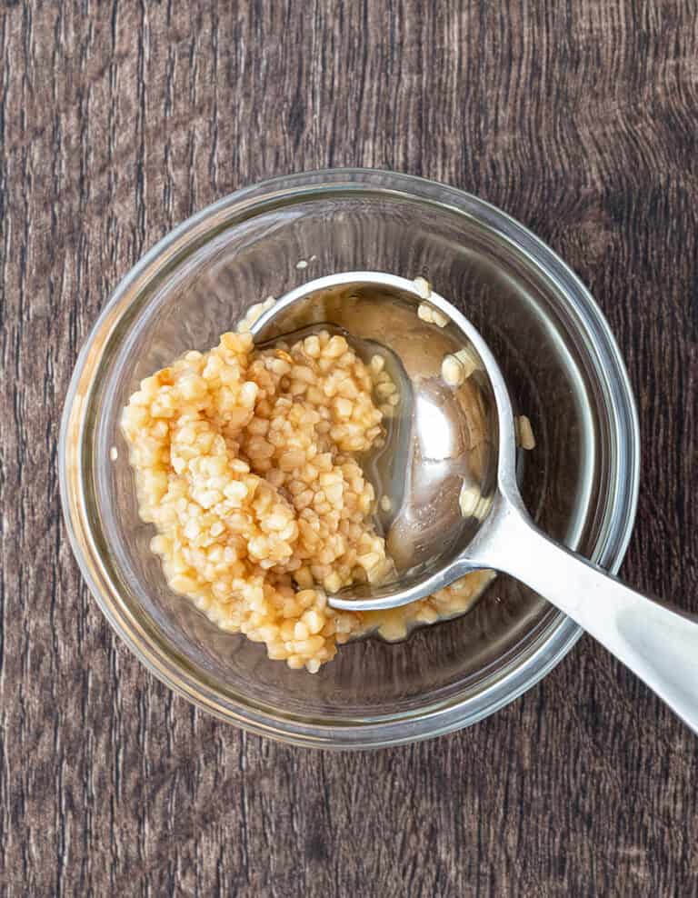 Minced Garlic in a Bowl with Spoon on Dark Wooden Surface
