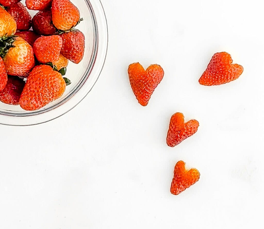 Strawberry Hearts on White Cutting Board with Bowl of Strawberries