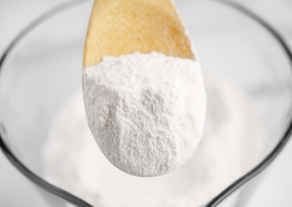 Powdered Sugar on Wooden Spoon with Glass Measuring Cup in Background