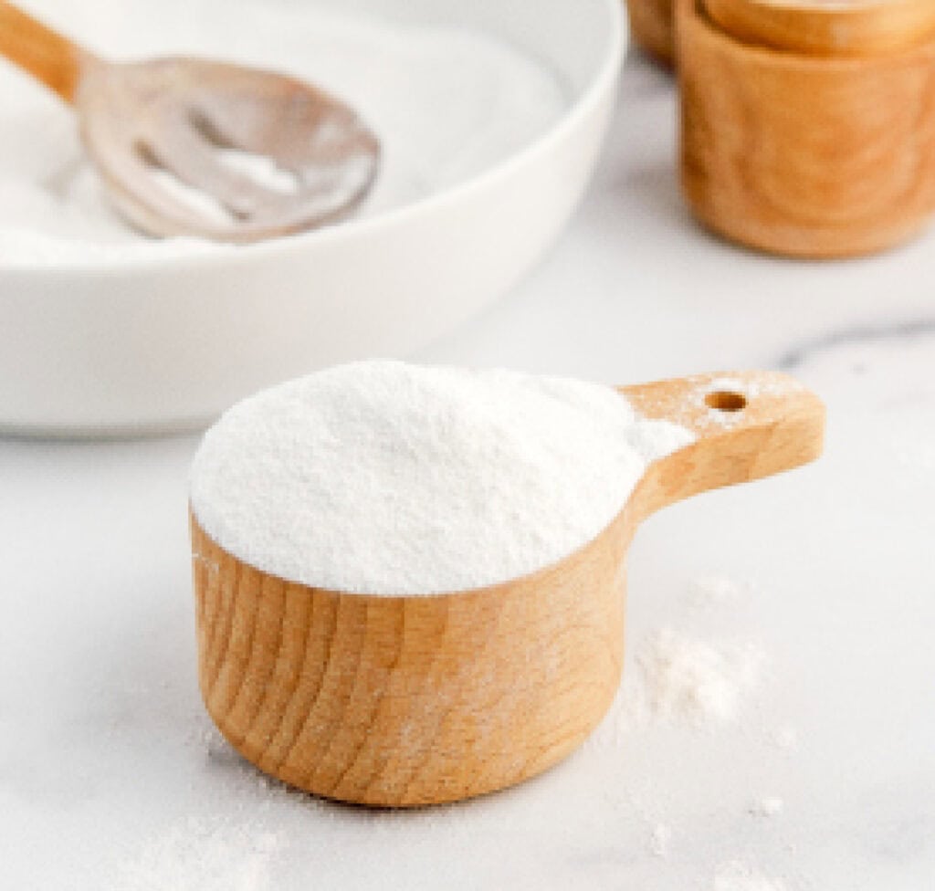 Powdered Sugar in Wooden Measuring Cup with Bowl of Powdered Sugar in Back with Wooden Spoon