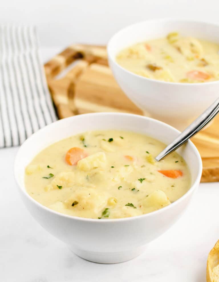 Knoephla Soup in White Bowl with Second Bowl Behind on Cutting Board