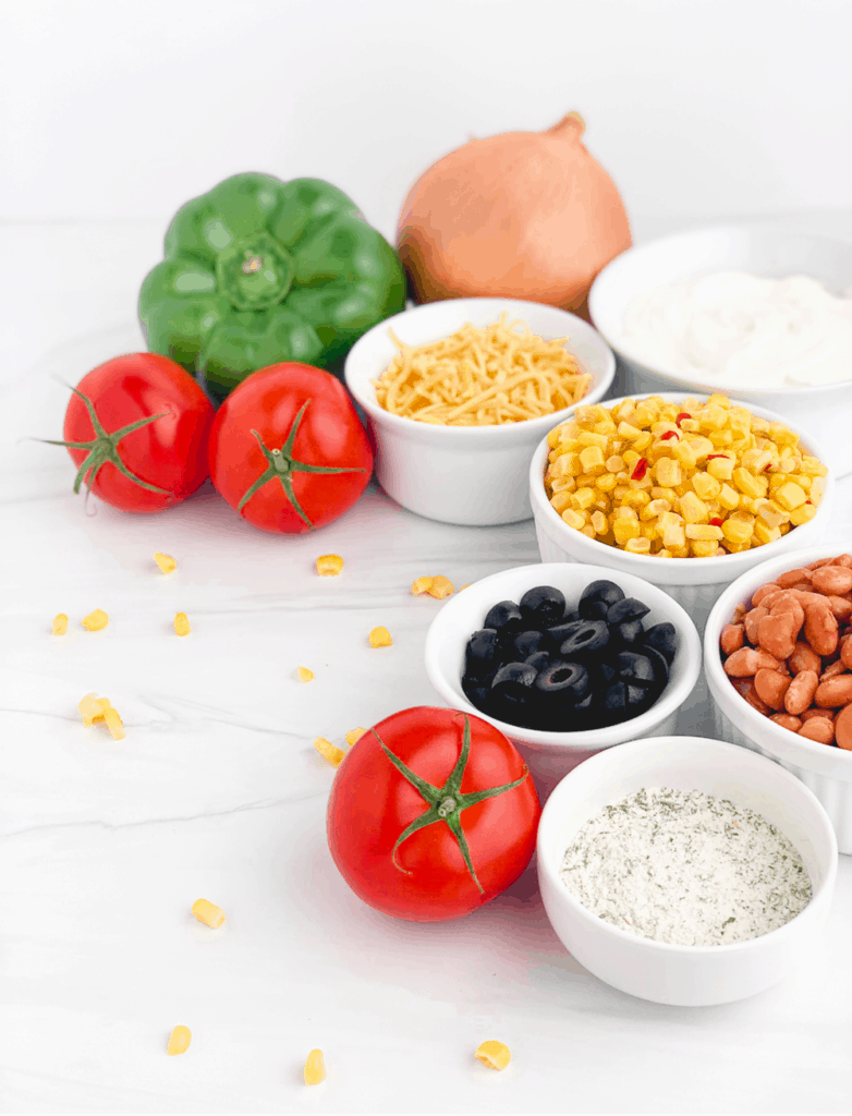 Mexicorn Dip Ingredients with Peppers, Tomatoes, Mexicorn, Pinto Beans, Sour Cream, Ranch Seasoning, Cheese, and Olives