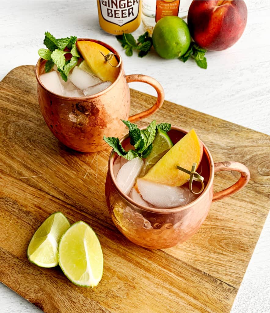 Peach Moscow Mules with Garnishes on Wooden Cutting Board with Lime Wedges