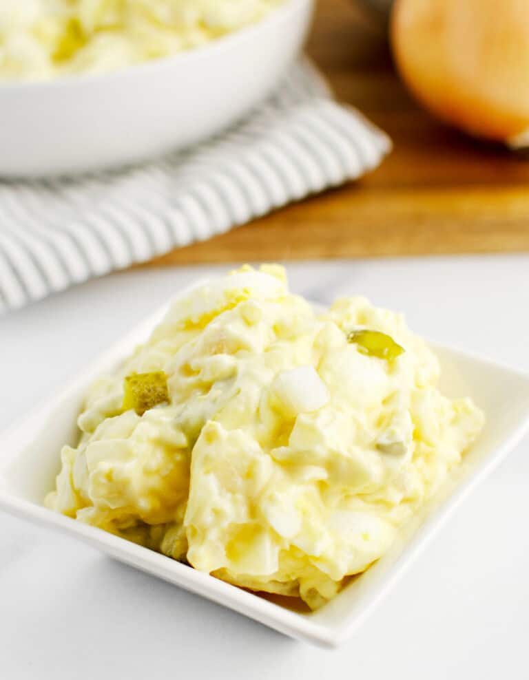 Potato Salad in a Square Bowl with Bowl and Kitchen Towel in the Background