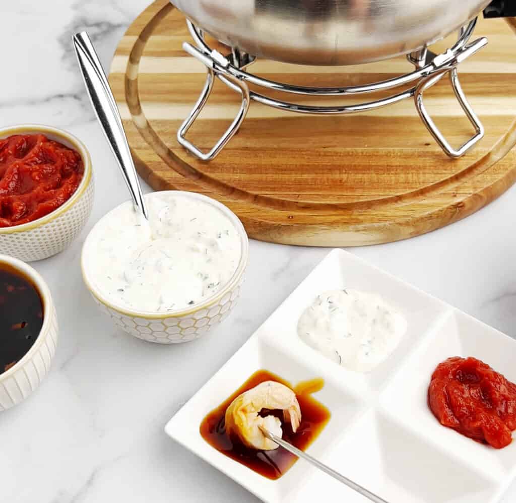 Closeup of Fondue Pot of Flavored Broth with Bowl of Raw Shrimp, Dipping Sauces, Fondue Forks, Plate with Sauces