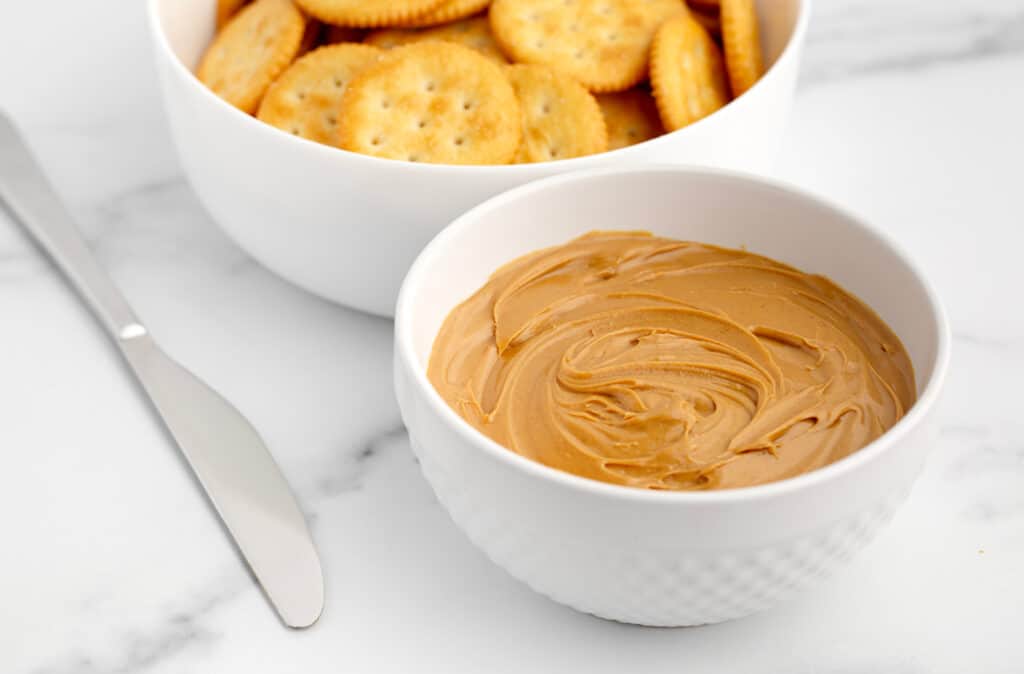 Bowl of Peanut Butter and Crackers with Knife on Marble Surface