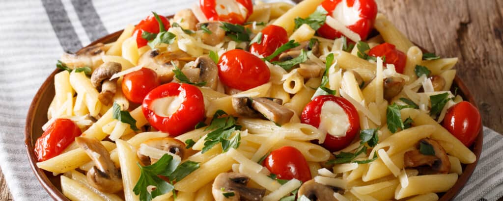 Bowl of Penne Pasta Topped with Cherry Peppers Mushrooms and Herbs