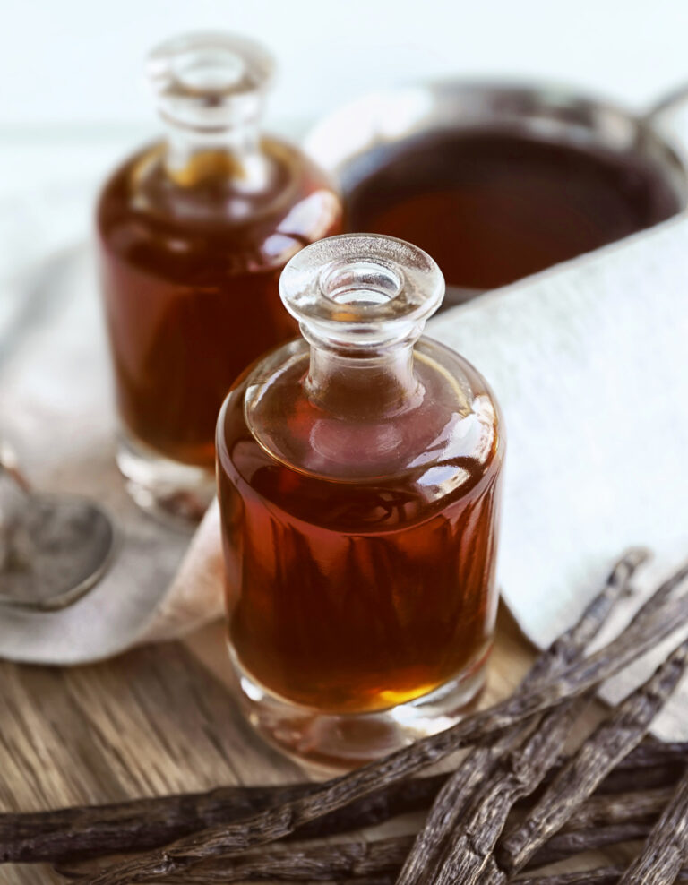 Jars of Vanilla Flavoring with Vanilla Beans and Towel on Wooden Surface