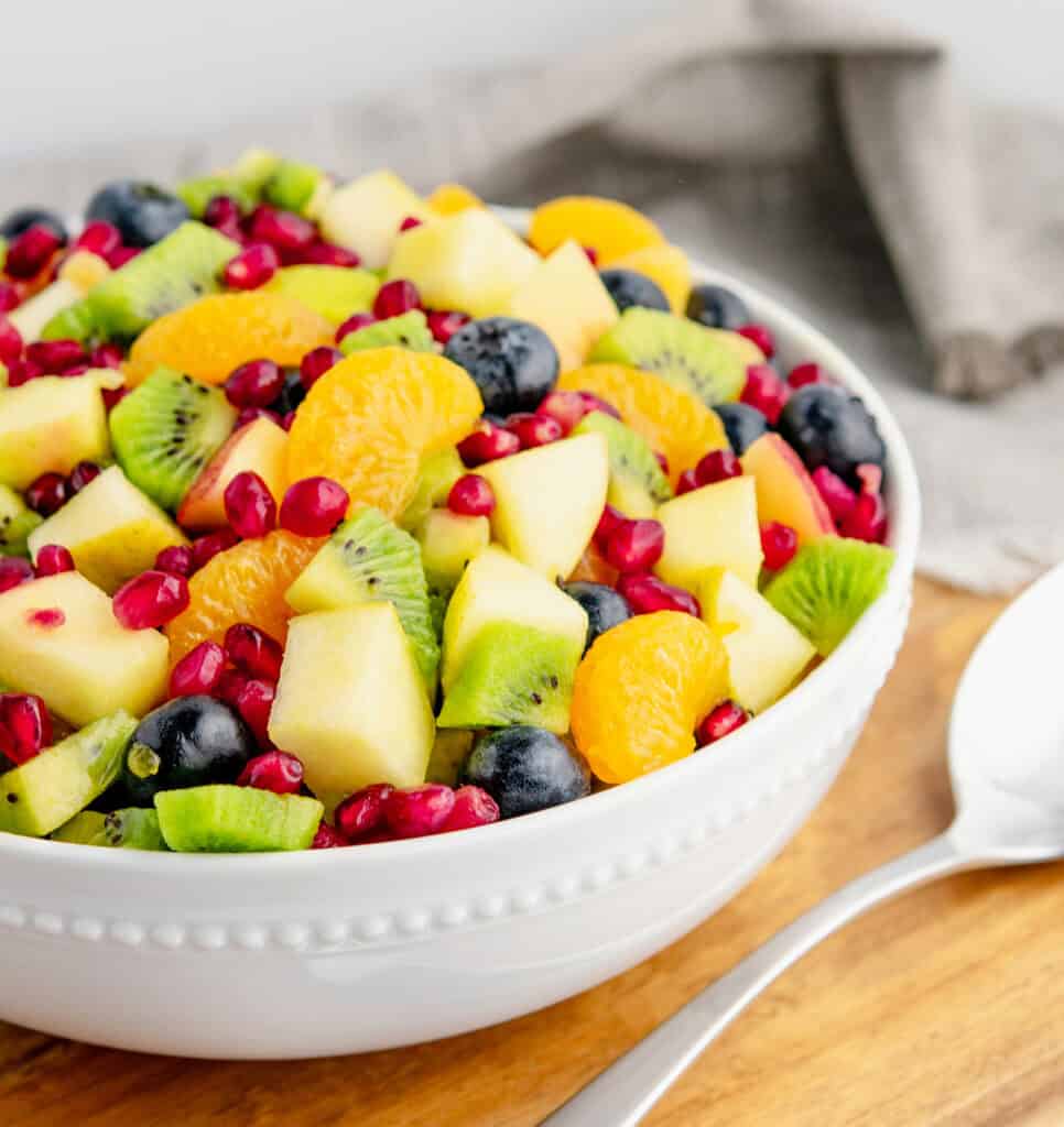 Winter Fruit Salad in White Bowl on Wooden Surface with Serving Spoon