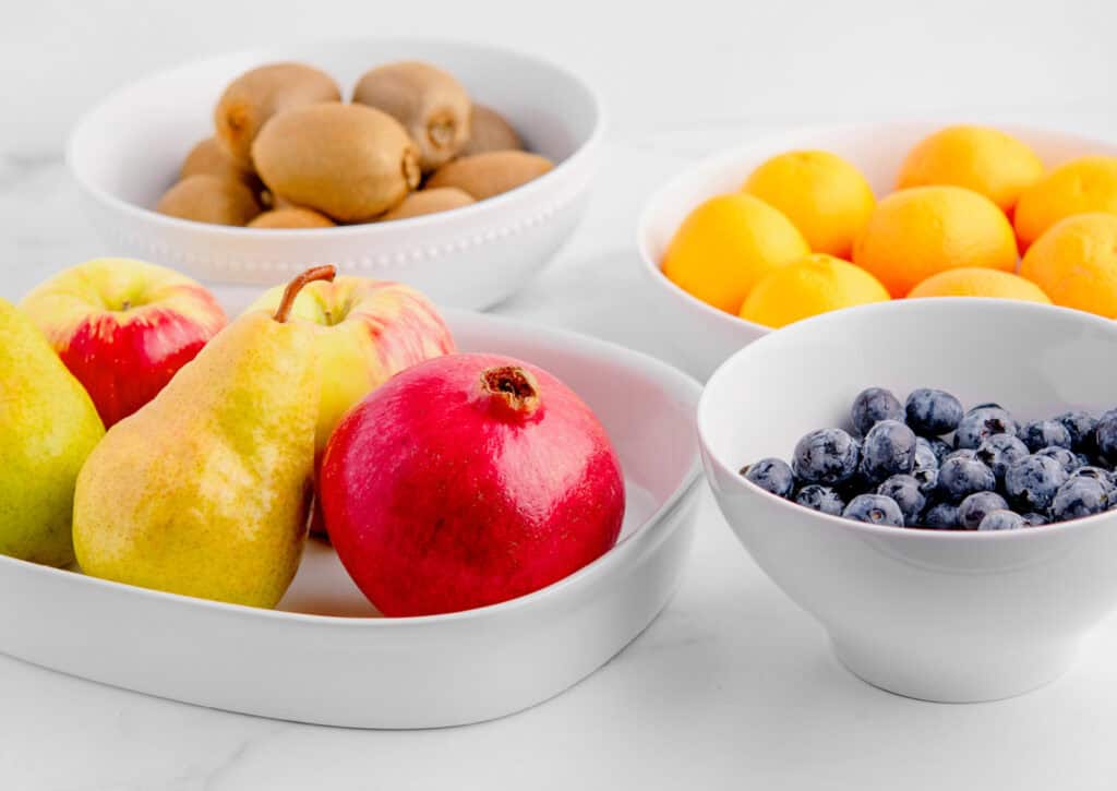 Kiwis, Mandarin Oranges, Pears, Apples, Pomegranates, and Blueberries in White Bowls